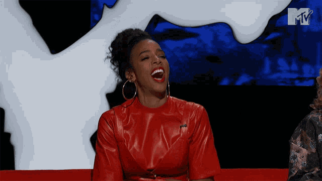 a woman in a red leather dress is laughing in front of a mtv sign