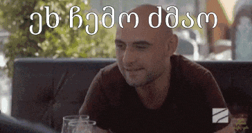 a man is sitting at a table with a glass of wine and a foreign language written on the bottom