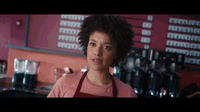 a woman wearing an apron is standing in front of a coffee machine in a coffee shop .