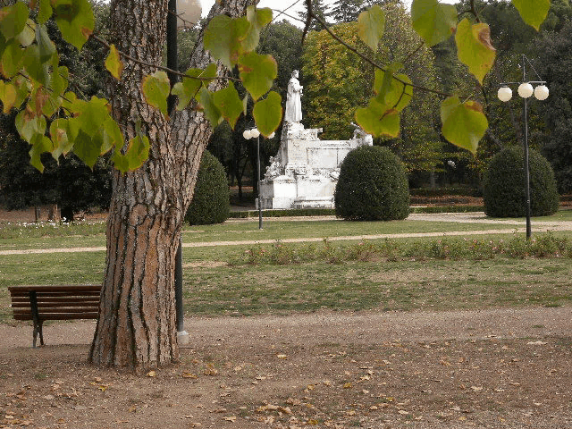 a park with a statue in the background and a bench in the foreground