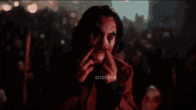 a man in a red suit and clown makeup is covering his mouth with his hands .