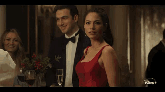 a woman in a red dress is standing next to a man in a tuxedo in a disney+ ad