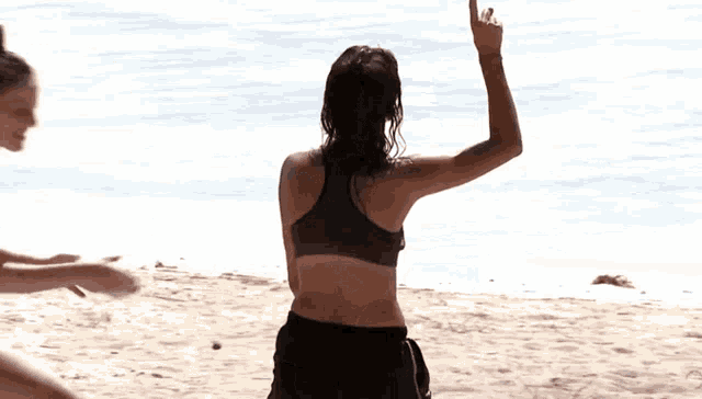 a woman in a bikini is standing on a beach with her hand in the air