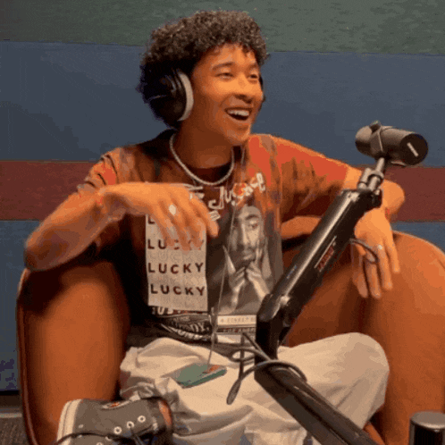 a man wearing headphones and a shirt that says lucky is sitting in front of a microphone