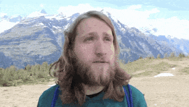 a man with long hair and a beard in front of a mountain
