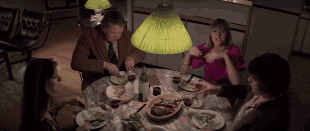 a group of people sitting around a table with plates of food and wine