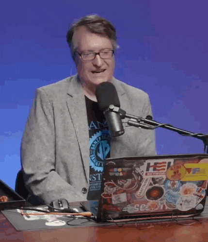 a man is sitting in front of a microphone and a laptop with stickers on it and the words i only wea behind him