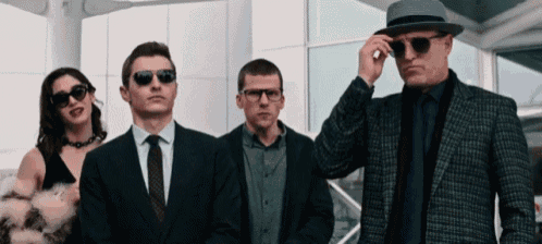 a man in a hat adjusts his sunglasses while standing next to two other men in suits and ties