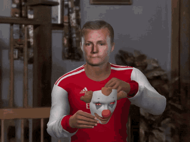 a man wearing a red emirates shirt holds a clown mask