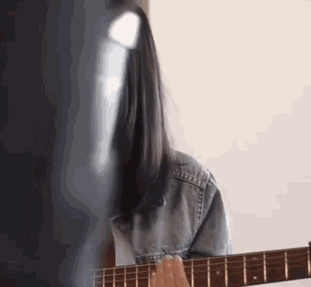 a woman with long black hair is playing an acoustic guitar .