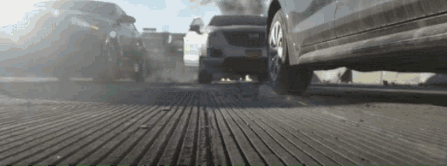 a row of cars are driving down a street with smoke coming out of their tires .
