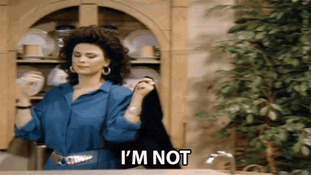 a woman in a blue shirt is saying i 'm not in front of a cabinet filled with plates .