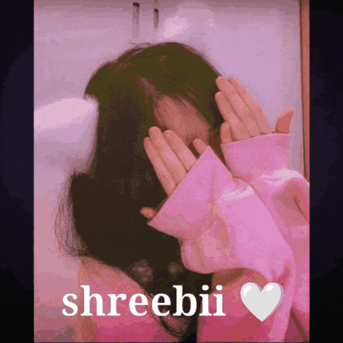 a girl in a pink sweater is covering her face with her hands and the name sreebii is on the bottom right