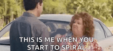 a man and a woman are standing next to each other in front of a car and talking to each other .
