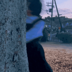 a person peeking out from behind a tree with a backpack