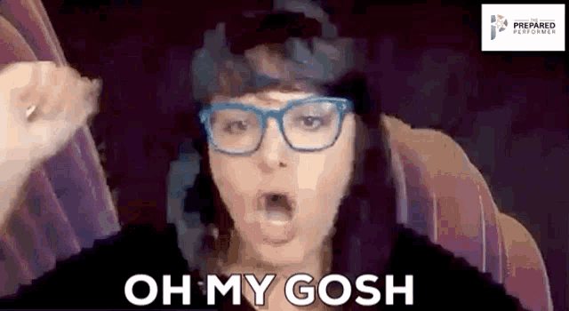 a woman wearing glasses is sitting in a chair with her mouth open and says oh my gosh .