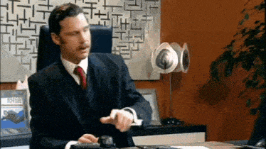 a man in a suit and tie is sitting at a desk using a calculator and a mouse .