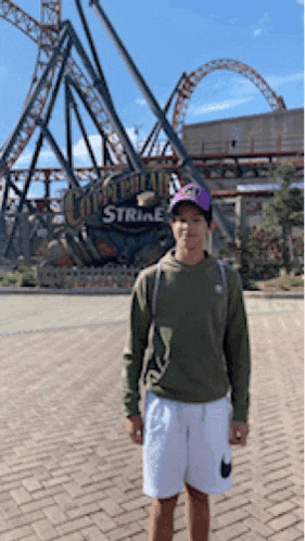 a young man is standing in front of a roller coaster called strike
