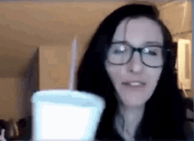 a woman wearing glasses is holding a white cup with a straw in her hand .