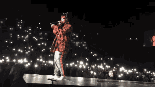 a man in a plaid shirt is singing into a microphone in front of a crowd
