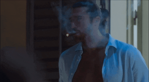 a shirtless man is smoking a cigar in front of a door .