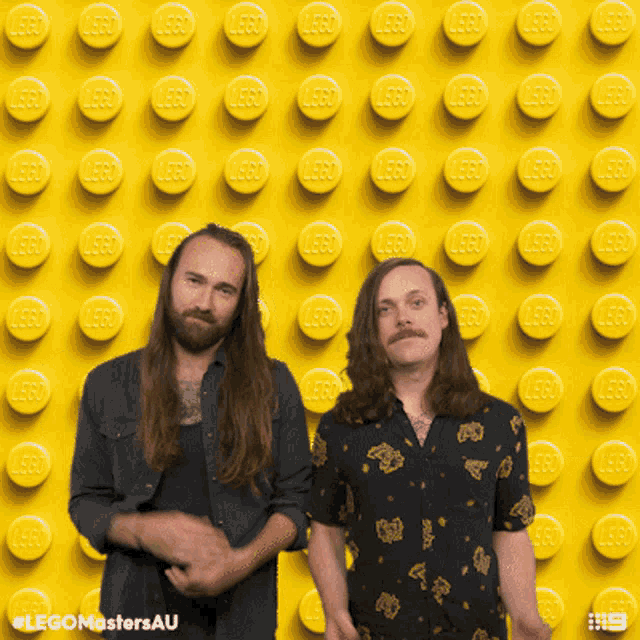 two men standing in front of a wall made of lego bricks