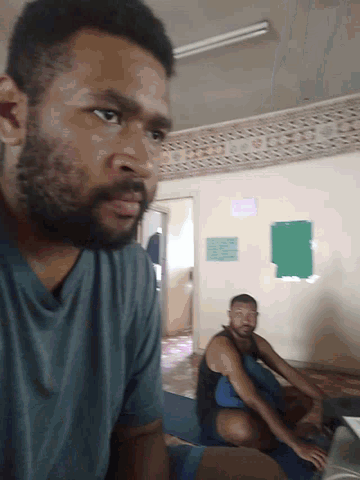 a man with a beard looks at the camera with a green sign on the wall behind him that says ' a '
