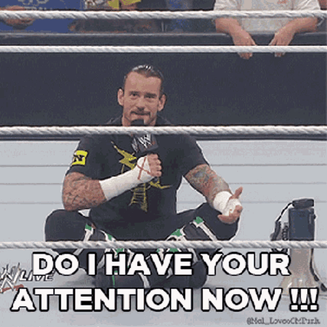 a man sitting in a wrestling ring holding a microphone with the caption do i have your attention now