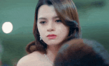 a close up of a woman wearing a necklace and earrings looking at the camera .