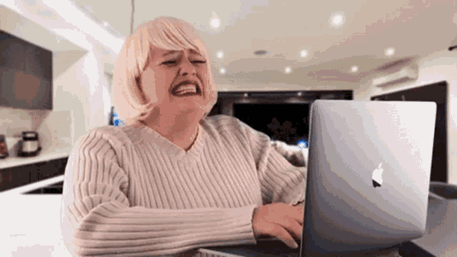 a woman in a white sweater is sitting at a table with an apple laptop .