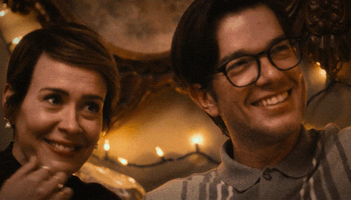 a man and a woman are smiling in front of christmas lights