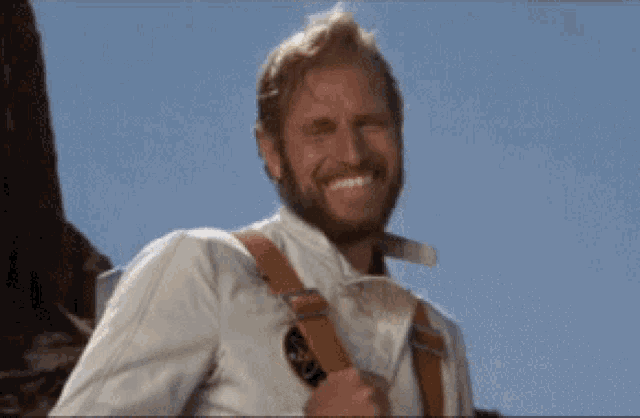 a man with a beard wearing suspenders and a white shirt is smiling
