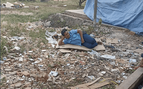a man in a blue shirt is laying on a cardboard box on the ground