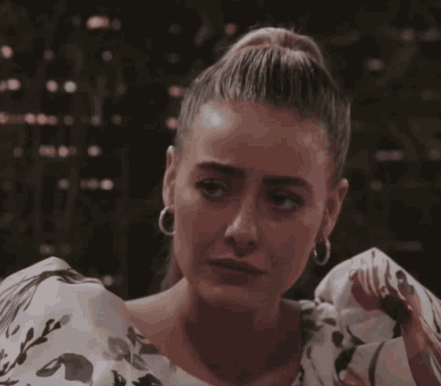 a woman wearing hoop earrings and a floral top is looking down