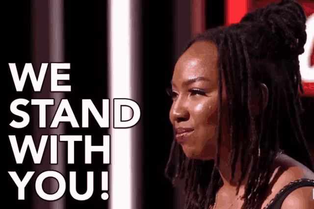 a woman with dreadlocks stands in front of a sign that says `` we stand with you '' .