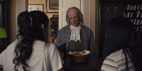 a man with gray hair is talking to two women while holding a basket of bread