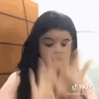 a girl is covering her face with her hands while making a funny face .