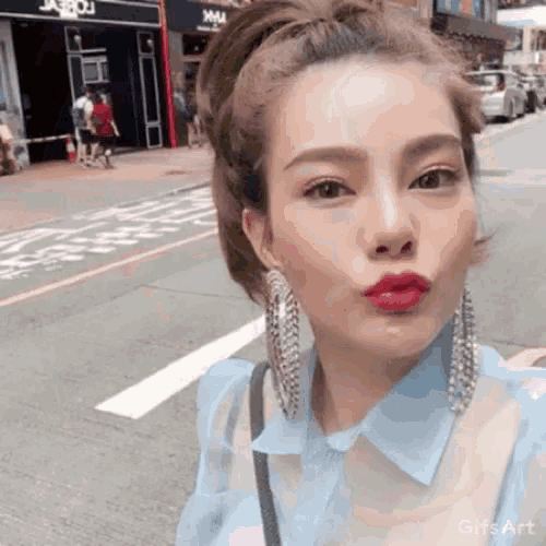 a woman wearing a blue shirt and earrings is making a funny face on the street .