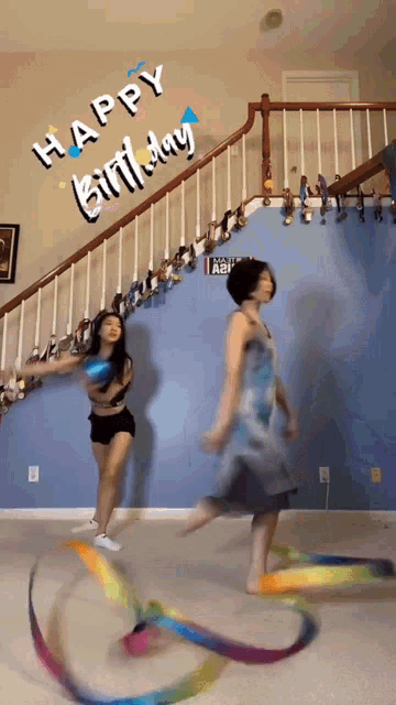 two women are dancing in front of a blue wall that says happy birthday on it