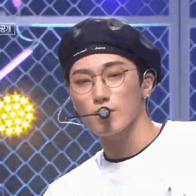a young man wearing glasses and a beret with a microphone in his mouth