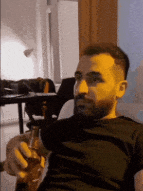 a man with a beard is sitting on a couch drinking a beer