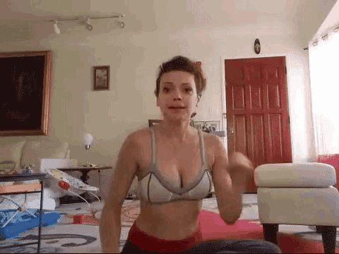 a woman in a sports bra is doing exercises on a yoga mat in a living room .