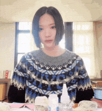 a woman wearing a sweater with a blue and white pattern looks at the camera