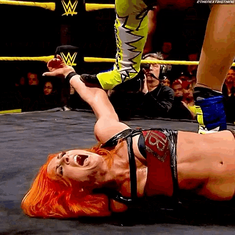 a woman is laying on the ground in a wrestling ring with a w logo on the wall