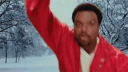 a man in a red jacket is standing in the snow with his arms in the air .