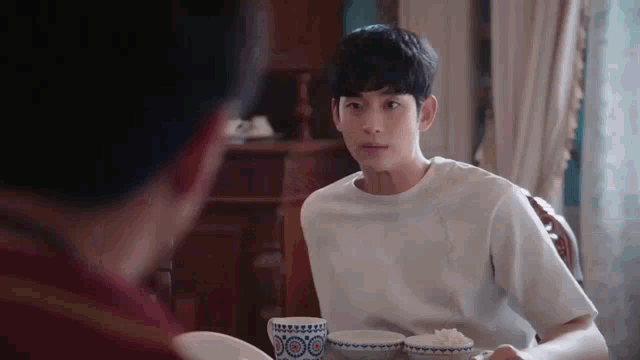 a young man is sitting at a table with bowls of rice and a cup of coffee .