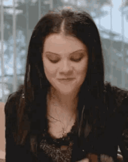 a woman with long black hair is sitting at a table making a funny face .