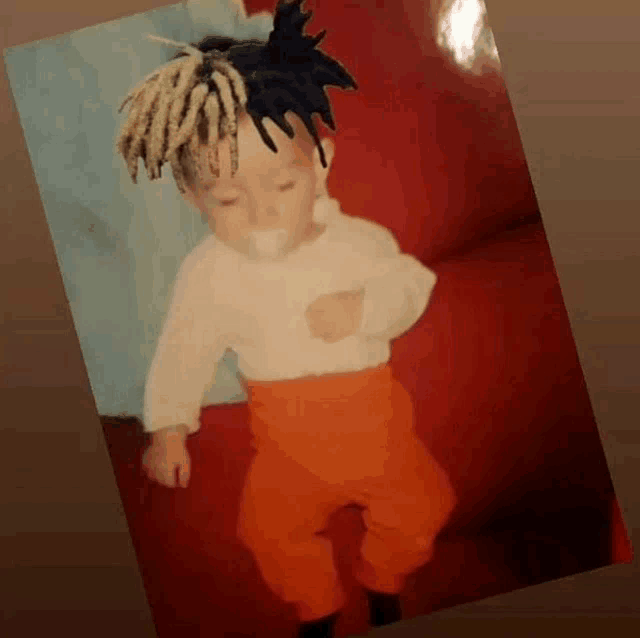 a baby with dreadlocks and orange pants is standing on a couch .