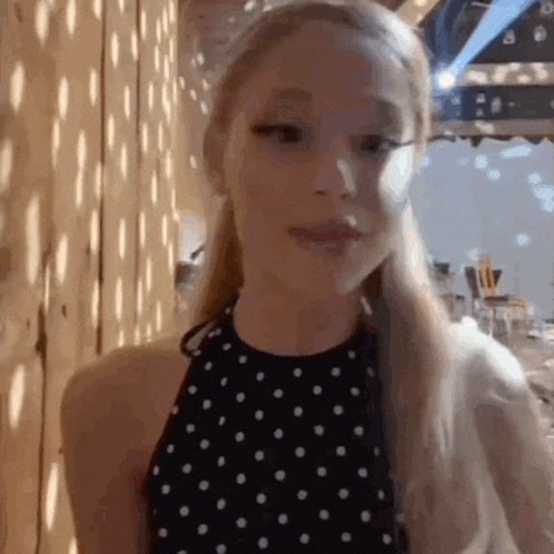 a woman in a black and white polka dot dress is standing in front of a wooden wall and looking at the camera .
