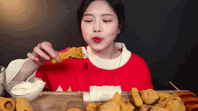 a woman in a red sweater is eating fried chicken with a fork .